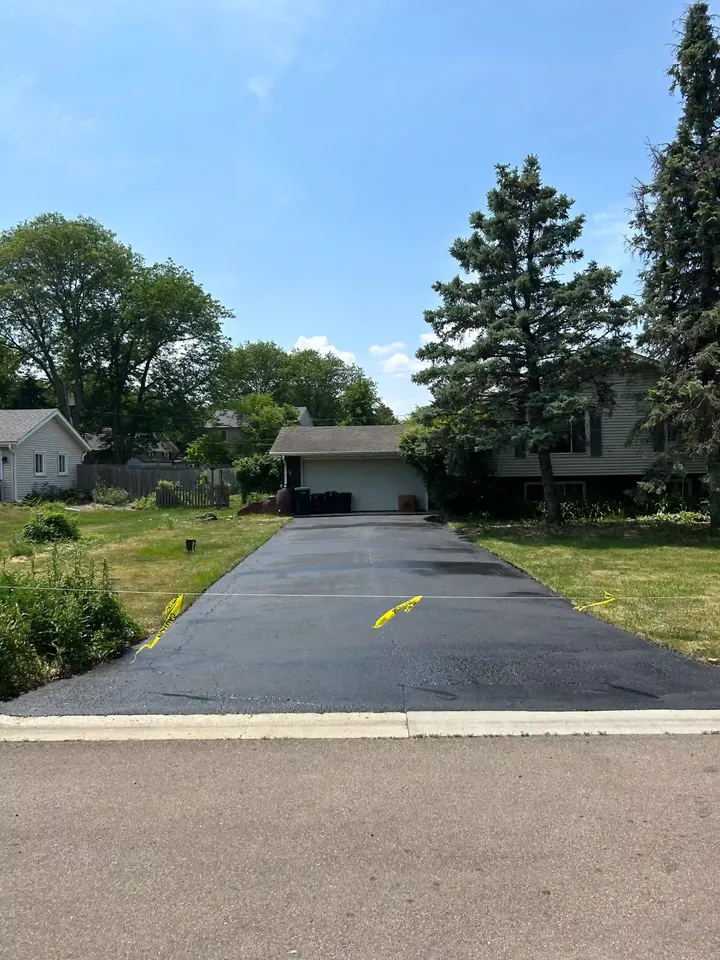 Completed dark driveway leading toward a detached garage beneath trees