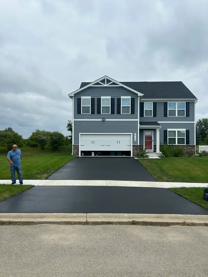 Coated driveway in front of a gray two-story home under an overcast sky