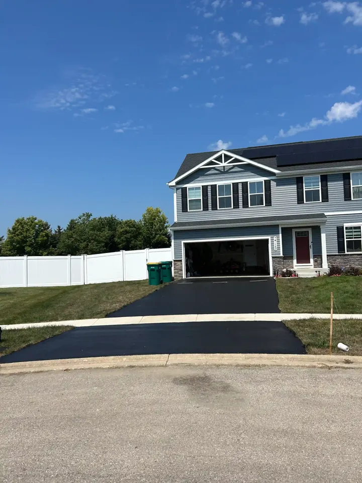 Sealcoated driveway outside a gray house, viewed from an angle across the street