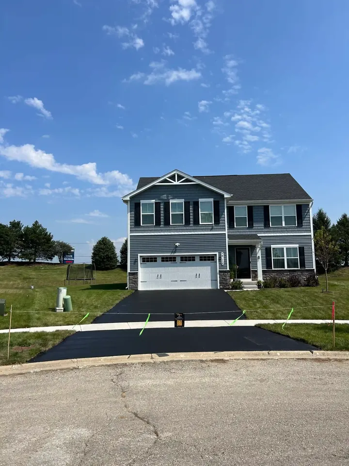 Dark driveway leading to a two-story home beneath a bright blue sky