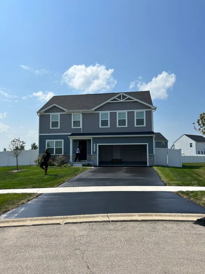Completed driveway in front of a gray house beneath passing clouds