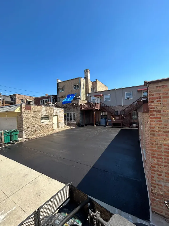 Dark asphalt area between brick buildings and a concrete walkway