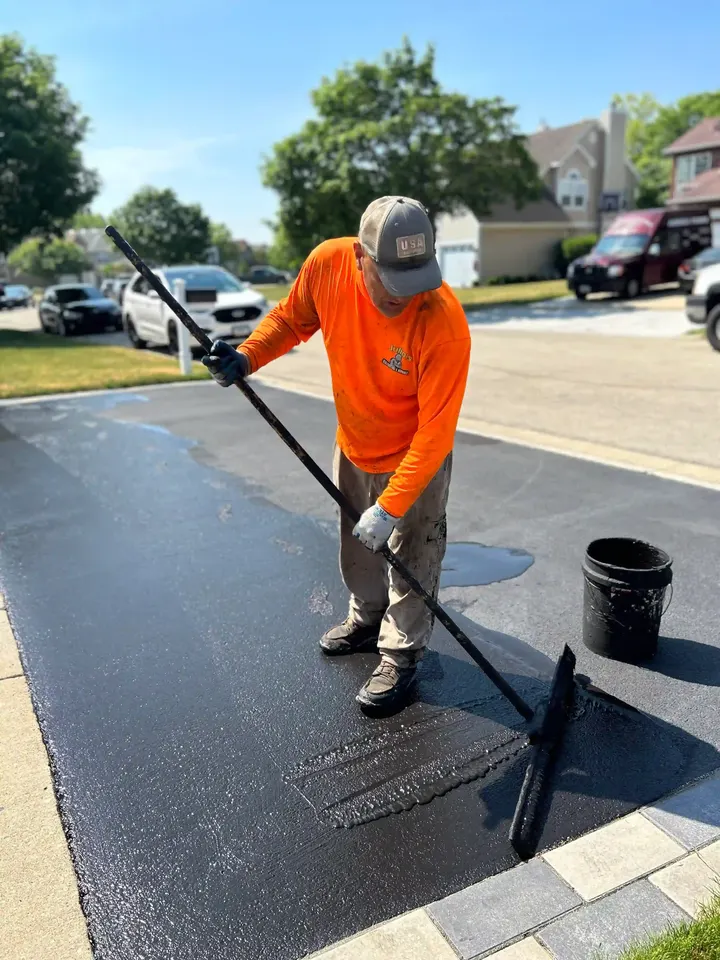 Crew member drawing a wide sealcoating brush across a driveway