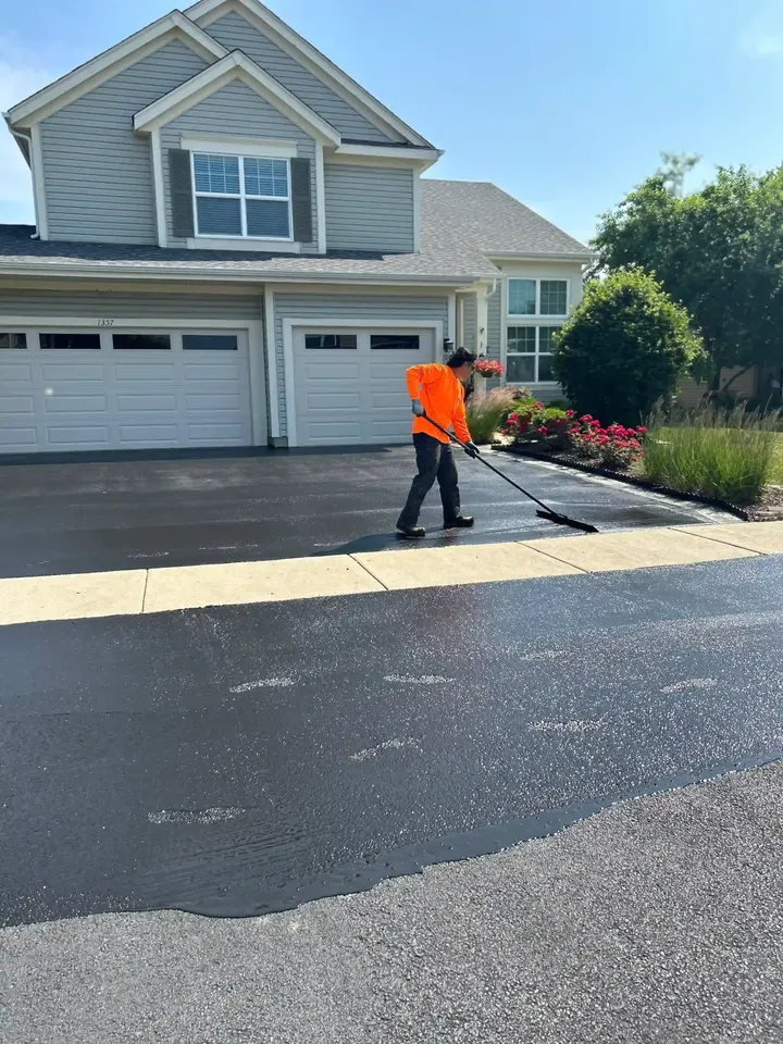 Crew applying sealcoat to a driveway outside a gray two-story home