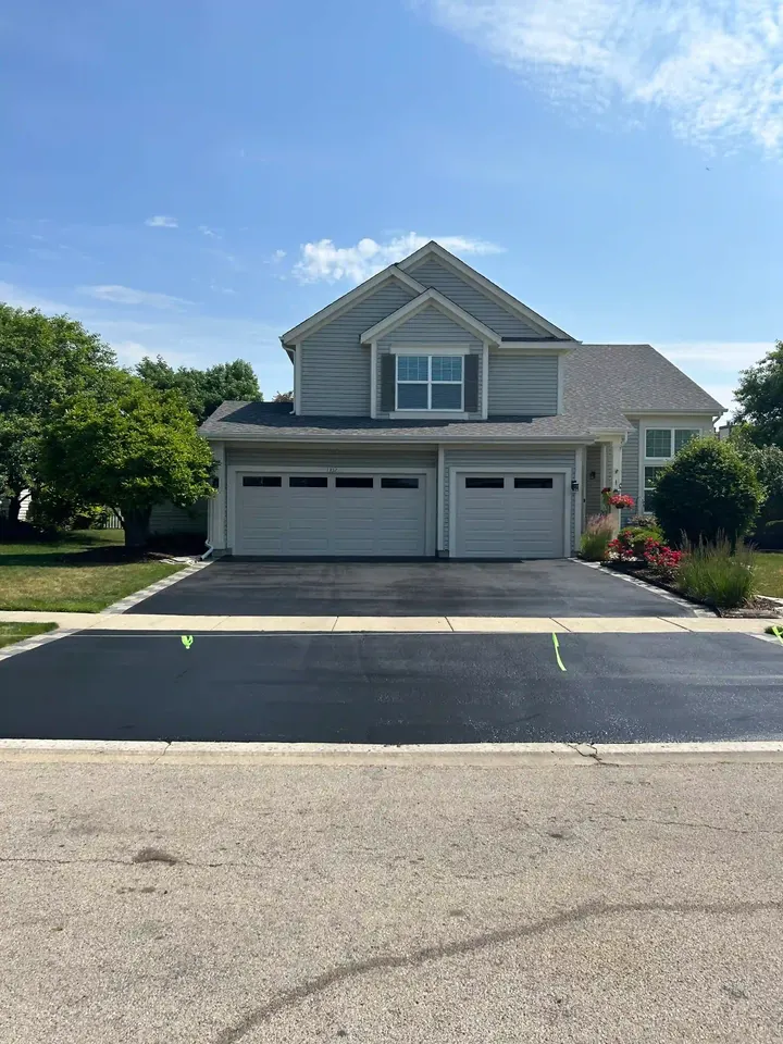 Finished driveway outside a gray home with yellow tape across the surface