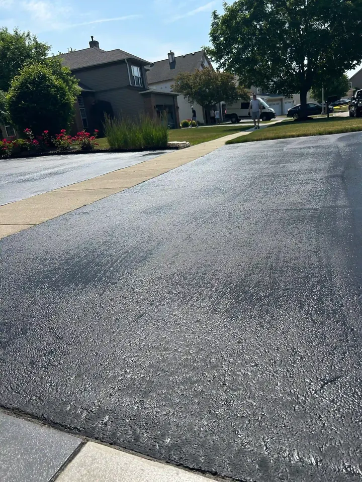 Low-angle view of coated driveway asphalt beside a concrete sidewalk