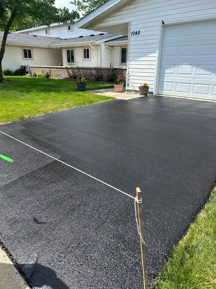 Dark driveway surface beside a white garage, blocked off with a cord