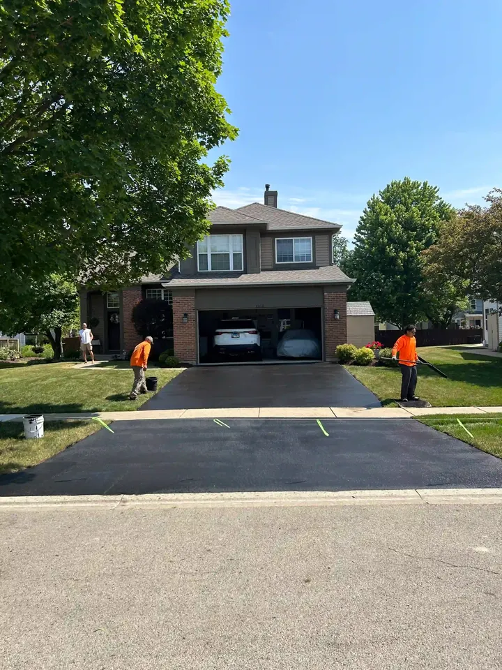 Two workers coating a driveway leading to an open garage