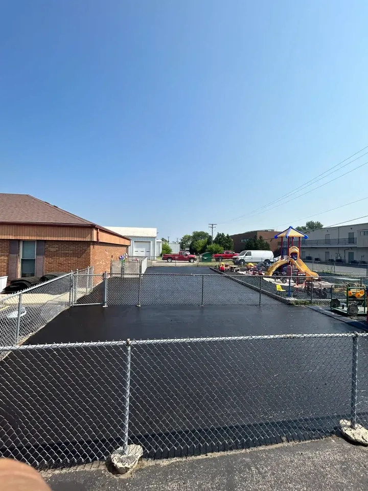 Dark paved area behind a chain-link fence beside brick buildings