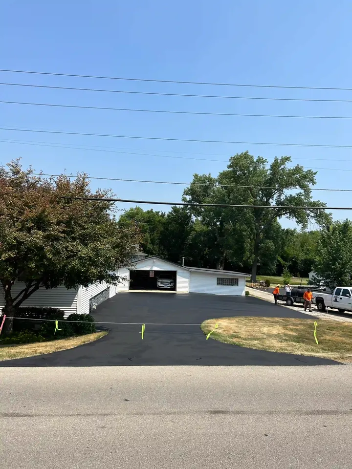 Broad asphalt driveway curving around a lawn toward a white garage
