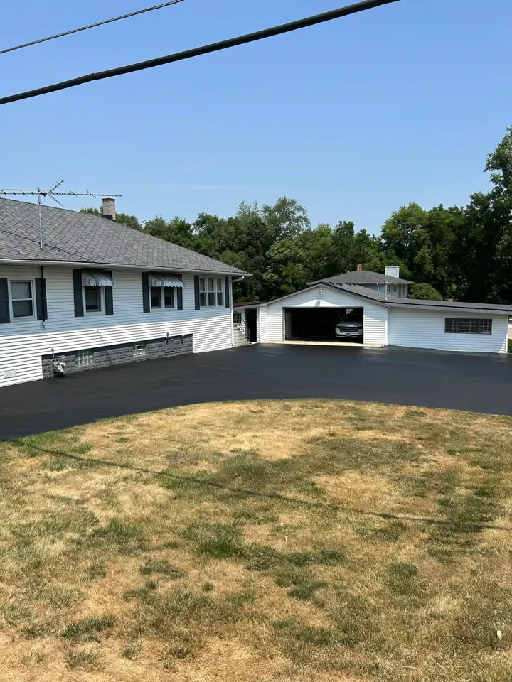 Coated curved driveway surrounding a lawn outside a white house