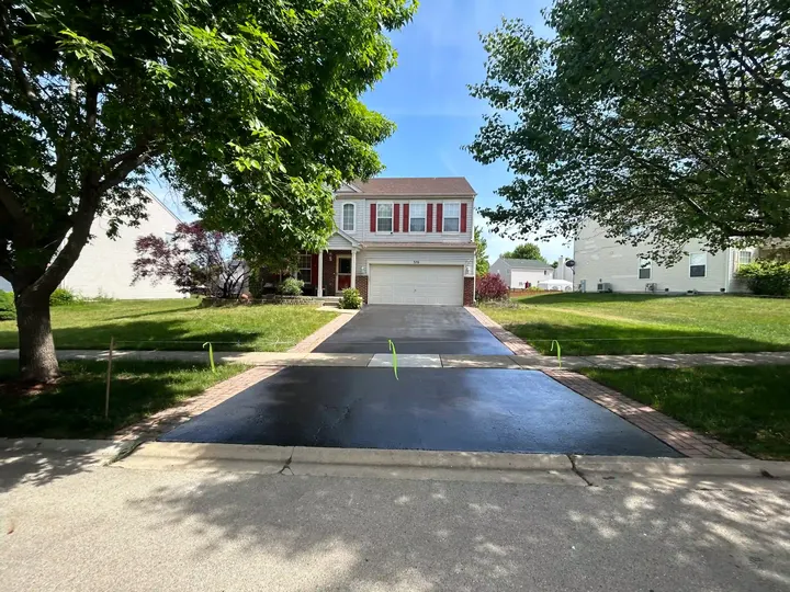 Sealcoated driveway leading from the street to a two-story home beneath trees