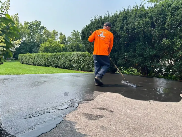 Crew member brushing sealcoat toward the edge of a driveway