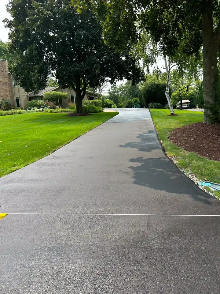 Long sealcoated driveway with trees and lawn along both sides
