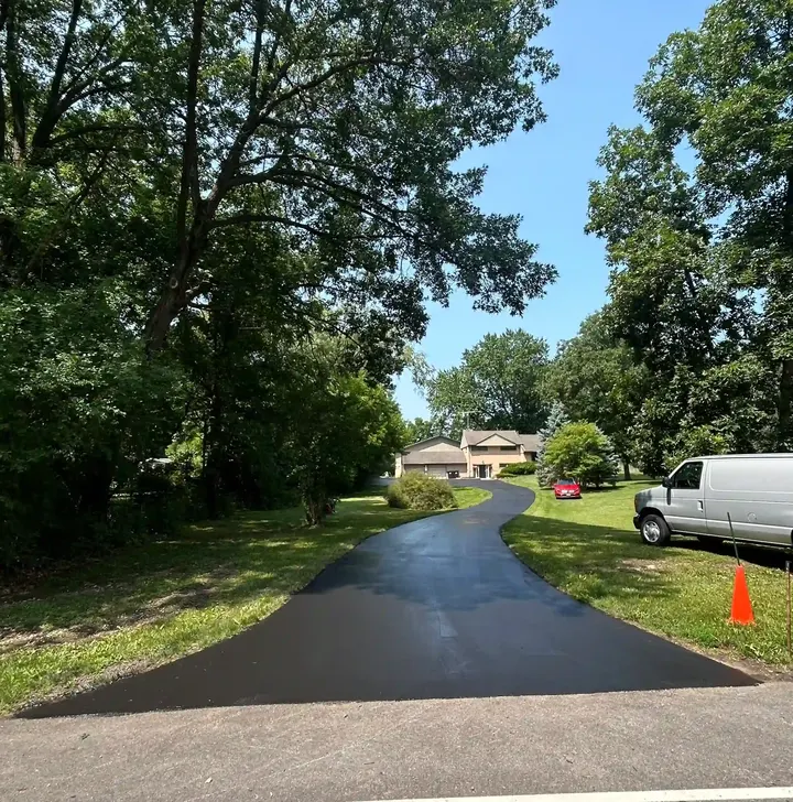 Curved dark driveway beside a lawn with an orange safety cone
