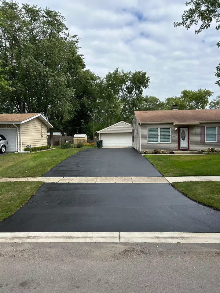 Finished driveway leading to a detached garage beside a low brick home