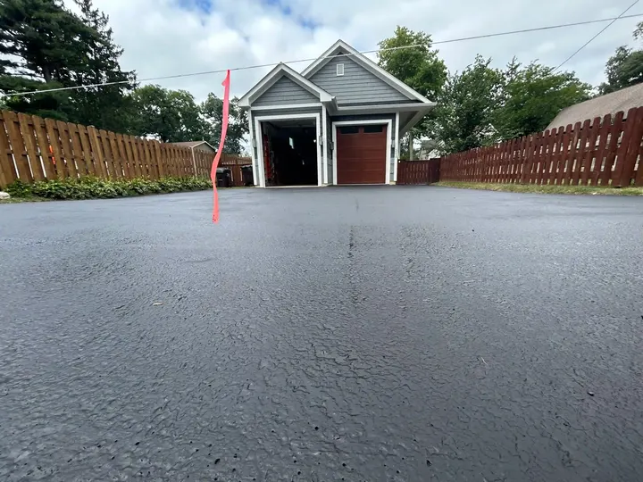 Low-angle view of coated asphalt leading to a detached garage between fences