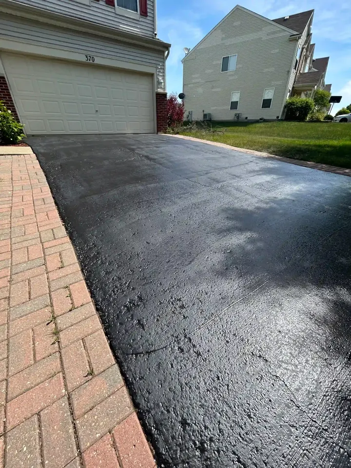 Freshly coated driveway with a brick edge beside a garage