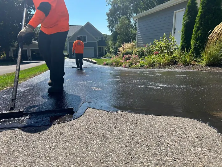 Two workers applying sealcoat along the edge of a driveway