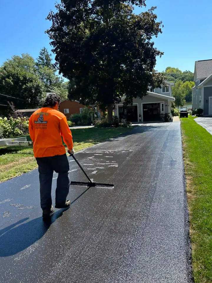 Crew member holding a wide brush on a freshly coated driveway