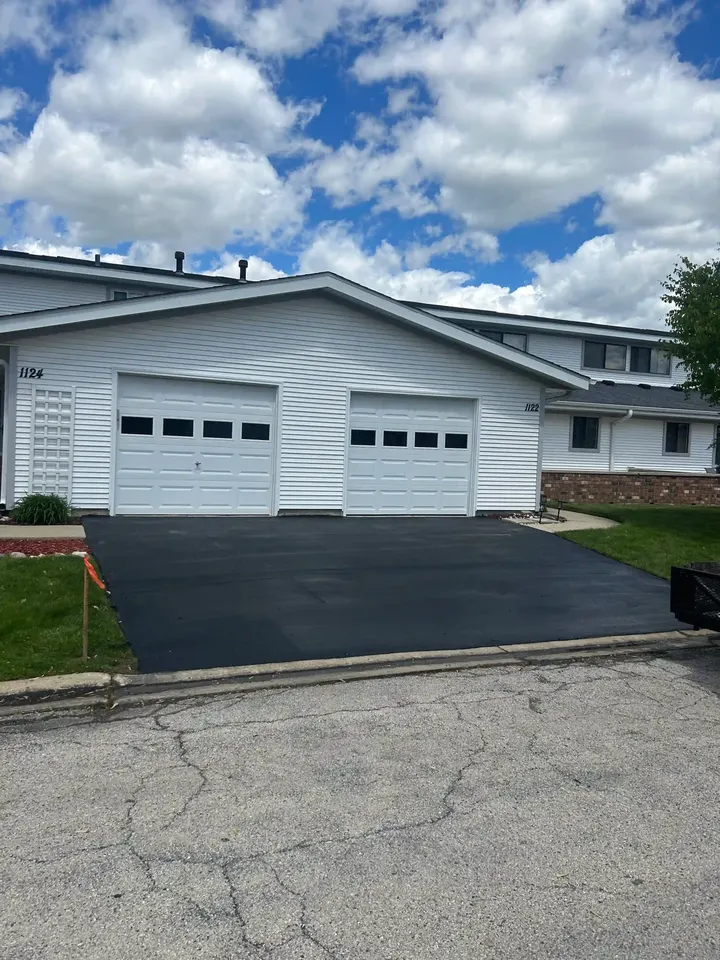Dark sloping driveway leading to a white two-car garage