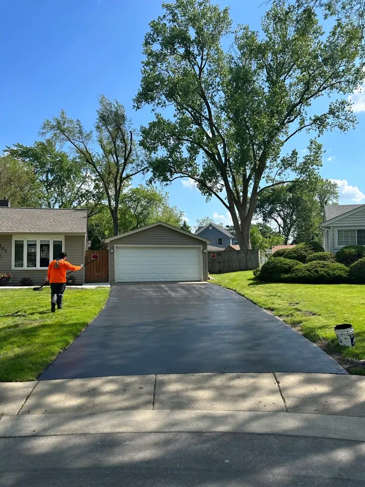 Crew member beside a coated driveway shaded by tall trees