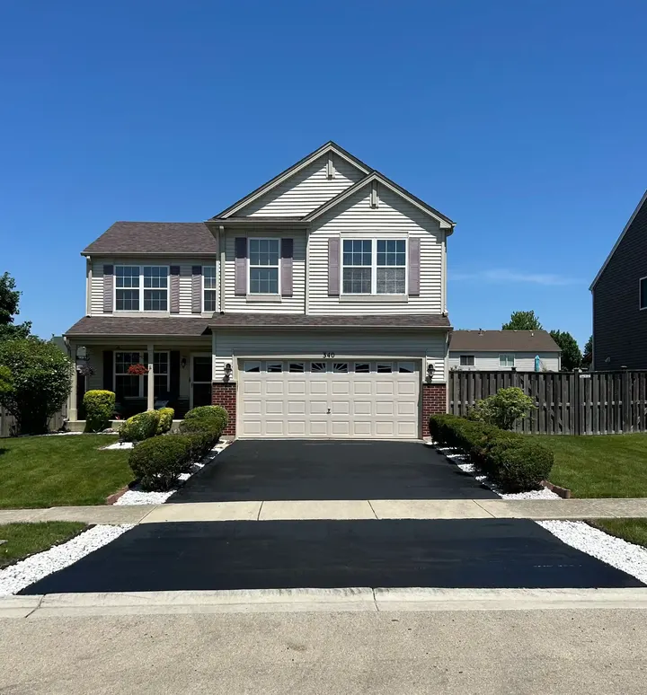Coated driveway and apron outside a tan two-story house