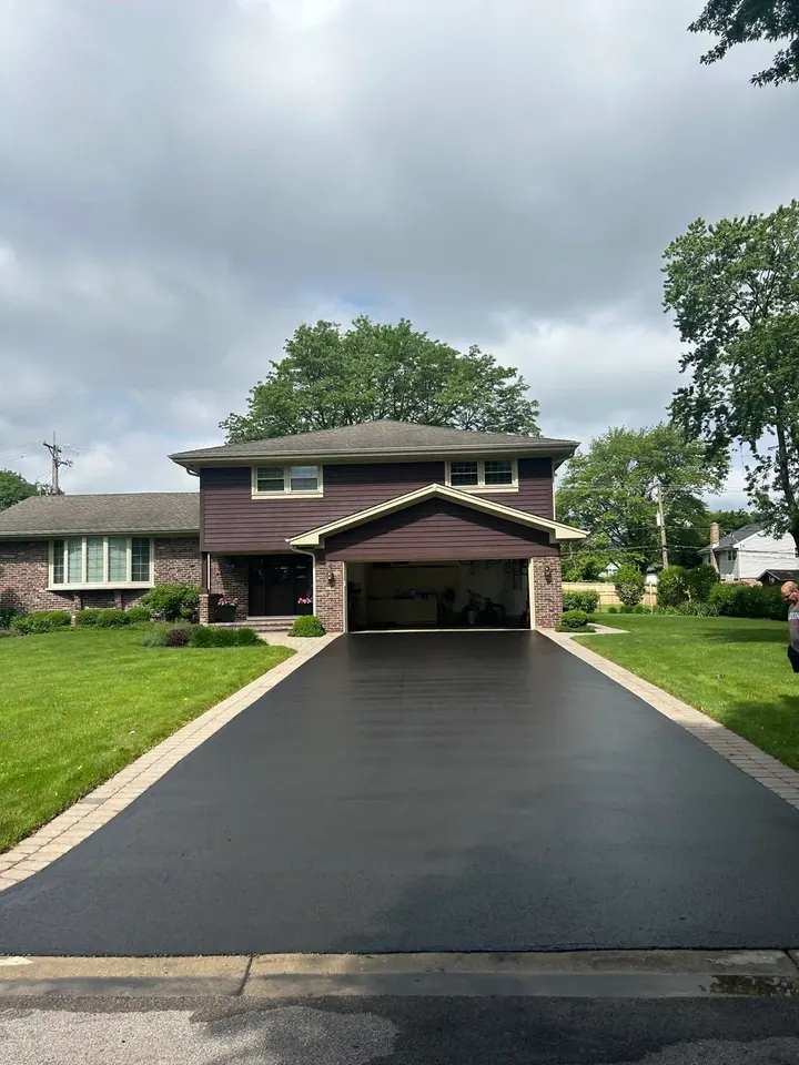 Dark driveway with clean edges leading toward a brown garage