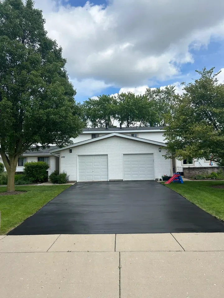 Coated driveway beneath a tree in front of a white garage