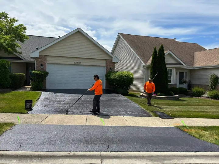 Two crew members spreading sealcoat across a driveway in front of a garage