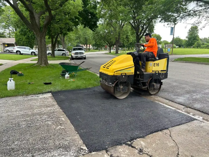 Worker operating a yellow roller on an asphalt repair near a sidewalk