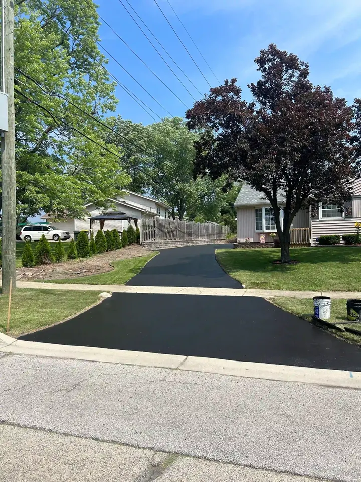 Straight dark driveway running beside a lawn and mature trees