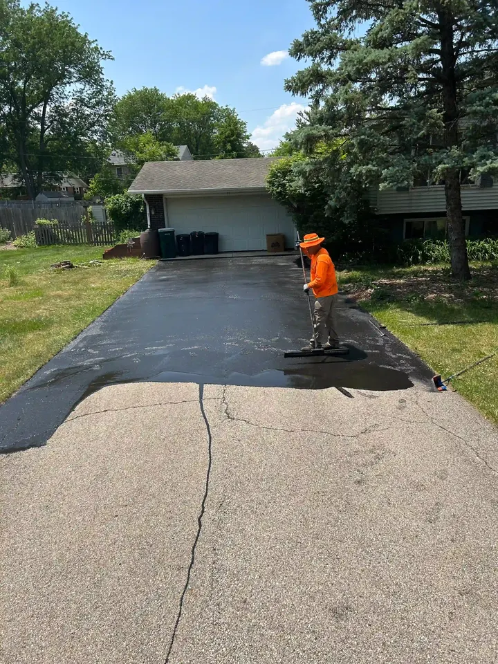 Worker applying sealcoat to the driveway entrance near the street