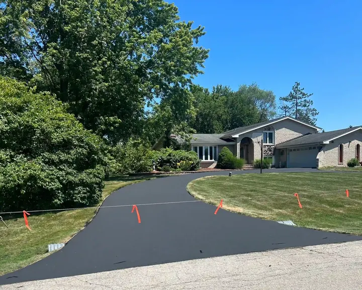 Curving driveway blocked off with flagged cord beside a green lawn