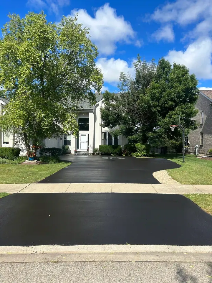 Dark driveway and apron in front of a tree-shaded home