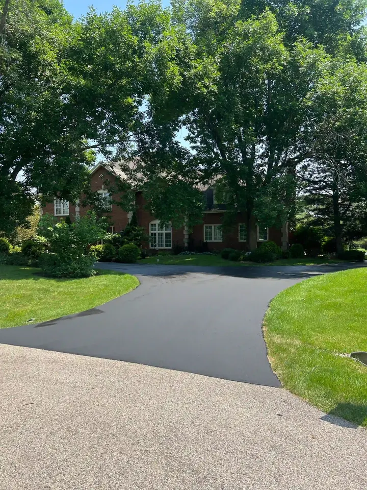 Curved sealcoated drive passing a grassy island outside a brick home